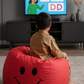 Child sitting on a red bean bag chair watching educational content on a TV.